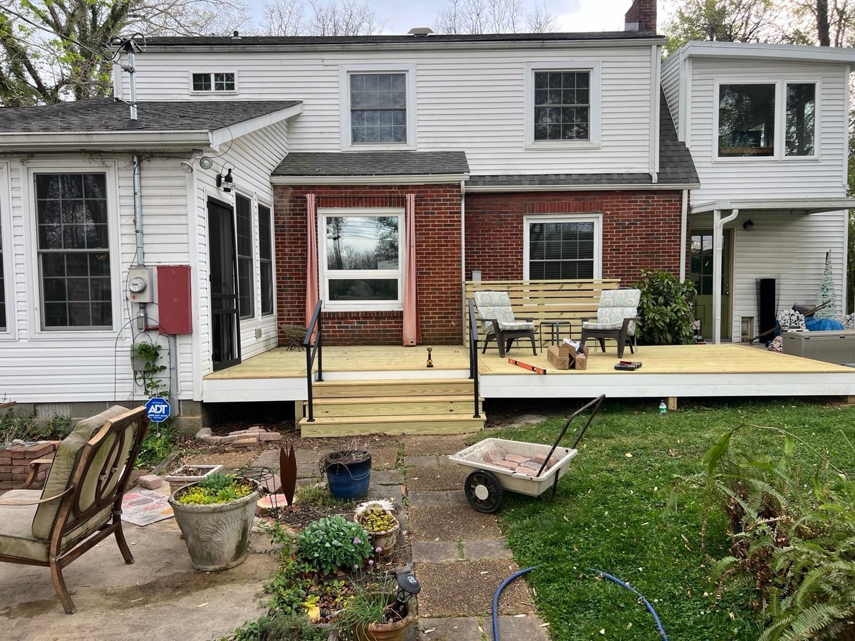 Backyard of brick and siding house with wooden deck, garden beds, lawn furniture, and potted plants