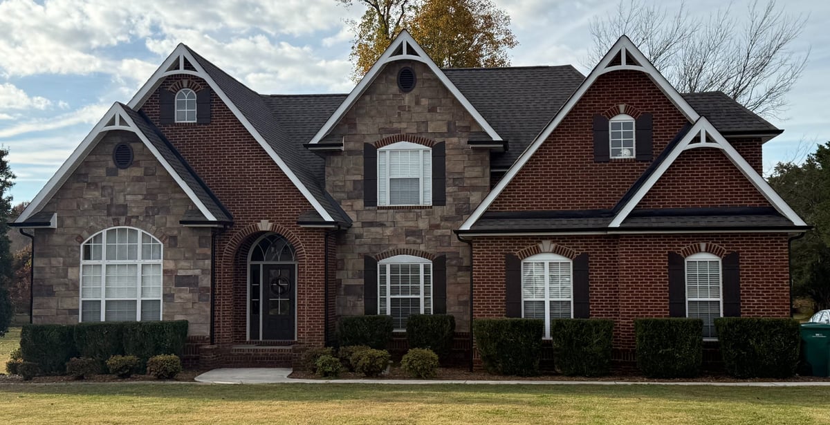 Two-story brick house with multiple peaked gables, white trim, and arched window on manicured lawn