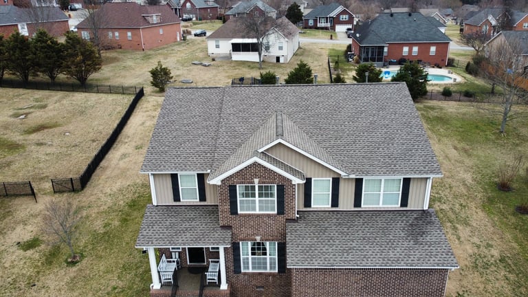 Aerial view of a two-story brick house with gray shingled roof and white trim in a residential neighborhood